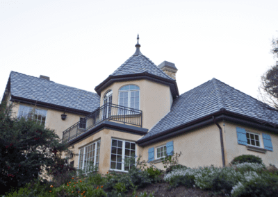 Large two-story house with a stucco facade and multiple gabled roofs, featuring a prominent turret with a conical roof.