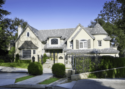 A gated two-story house with a landscaped front yard and a clear blue sky in the background.