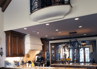 Elegant kitchen interior with wooden cabinets, a central island, chandelier lighting, and an upper level balcony with wrought iron railings.