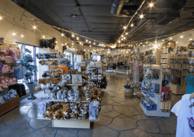 A gift shop interior with shelves displaying various plush toys, souvenirs, and decorative items. The ceiling is adorned with string lights.