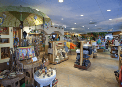 Inside a souvenir shop with various items displayed, including clothing, figurines, and colorful decorations. The store has wooden shelves and a warm, well-lit atmosphere.