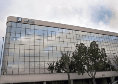 Glass-fronted office building with "Jacobs" signage at the top. Trees and a cloudy sky are reflected on the windows.