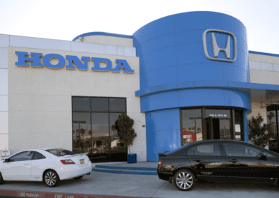 Exterior view of a Honda dealership with two cars parked in front, one white and one black.