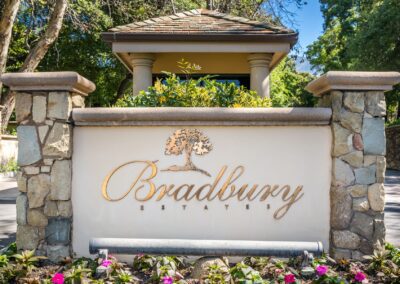 Entrance sign for Bradbury Estates featuring decorative stonework and a landscaped area with flowers in front.