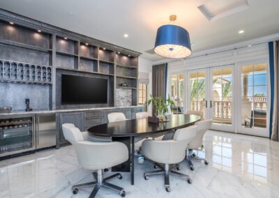 Modern conference room with a large oval table, eight white chairs, a built-in screen, shelves, a wine cooler, and glass doors leading to a balcony.