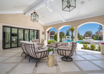 Luxurious outdoor patio with comfortable seating, arched openings, and a view of a pool and garden area.