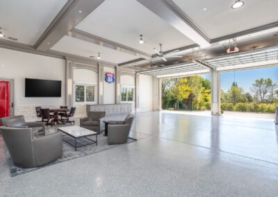 Spacious garage with seating area, large open door revealing greenery outside, a mounted TV, and Route 66 sign on the wall.