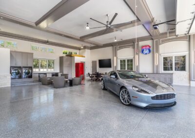 A luxury sports car is parked in a spacious, modern garage with seating area, laundry appliances, and vintage decor.