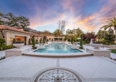 Luxurious backyard with a large pool, decorative planters, and elegant landscaping under a colorful sunset sky.