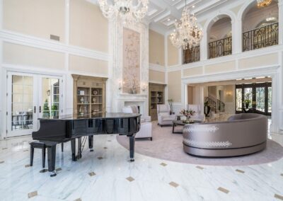 Spacious, elegant room with marble flooring, a grand piano, chandeliers, and a large curved sofa. High ceilings and decorative arches add to the sophisticated ambiance.