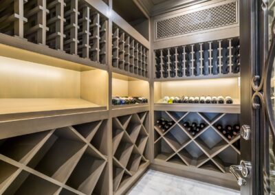 A wine cellar with wooden racks holding several bottles. The room is lit with built-in lighting and has a decorative door.