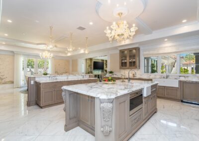 Luxurious kitchen with marble countertops, chandeliers, and wooden cabinetry. Large windows and high ceilings enhance the spacious layout.