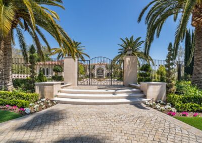 A gated entrance with curved steps, flanked by tall palm trees and manicured gardens, under a clear blue sky.