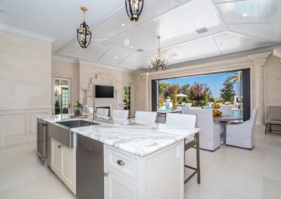 Spacious modern kitchen with marble countertops, stainless steel appliances, and a view of the backyard pool area through large open sliding doors.