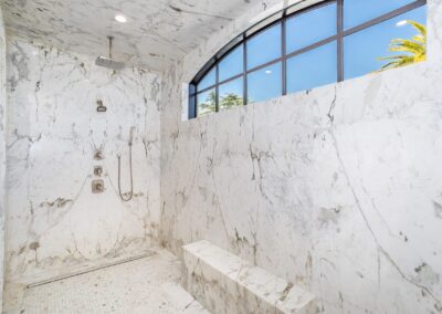 Luxurious marble shower with a large window, ceiling-mounted showerhead, and bench.