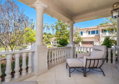 Elegant patio with cushioned chairs, stone balustrade, and a view of a lush garden and a two-story house.