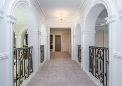 Elegant hallway with arched entryways, a chandelier, and ornate railings on a carpeted walkway.