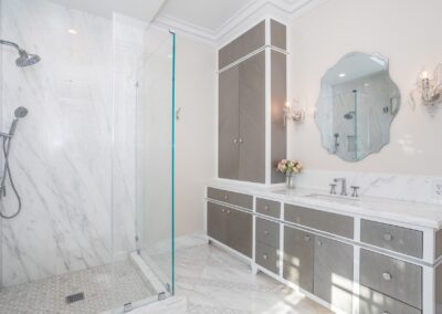 Modern bathroom with a glass shower, marble flooring, and a vanity with dual sinks. A decorative mirror and wall sconces are above the sinks.