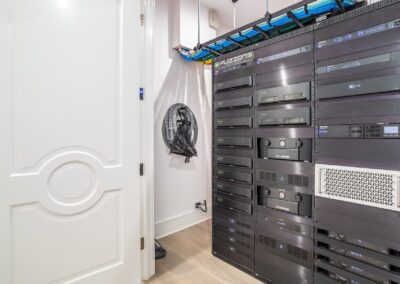 A modern server room with multiple black server racks, blue cable management, and a white paneled door on the left.