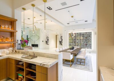 Luxurious modern kitchen and dining area with marble countertops, wooden cabinets, bright lighting, and contemporary decor, including a wine rack and artworks.