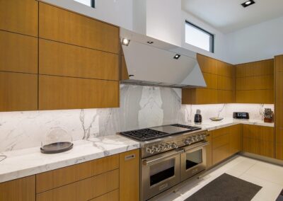 Modern kitchen with wooden cabinets, marble countertops, stainless steel appliances including a large stove and range hood, and under-cabinet lighting.